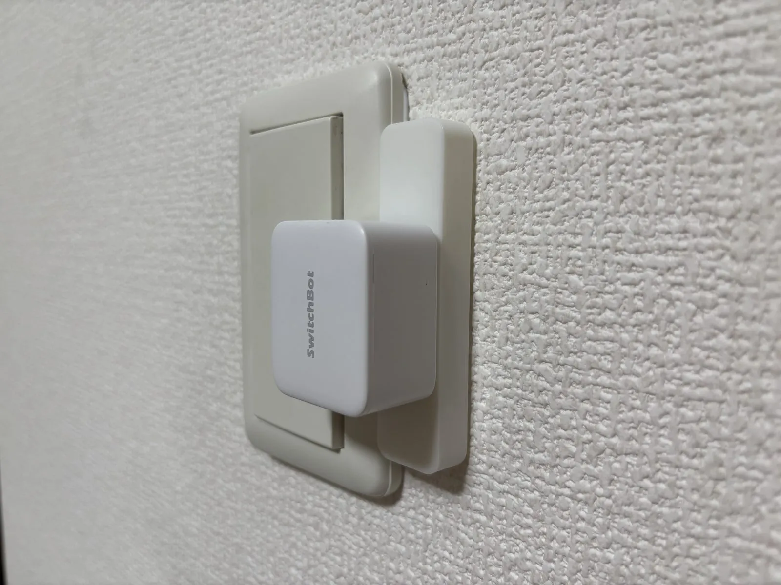 斜めから見たSmartBASE取付台。スイッチプレートの縁に被さる台座の上にボットが乗り、粘着テープに頼らず固定されている