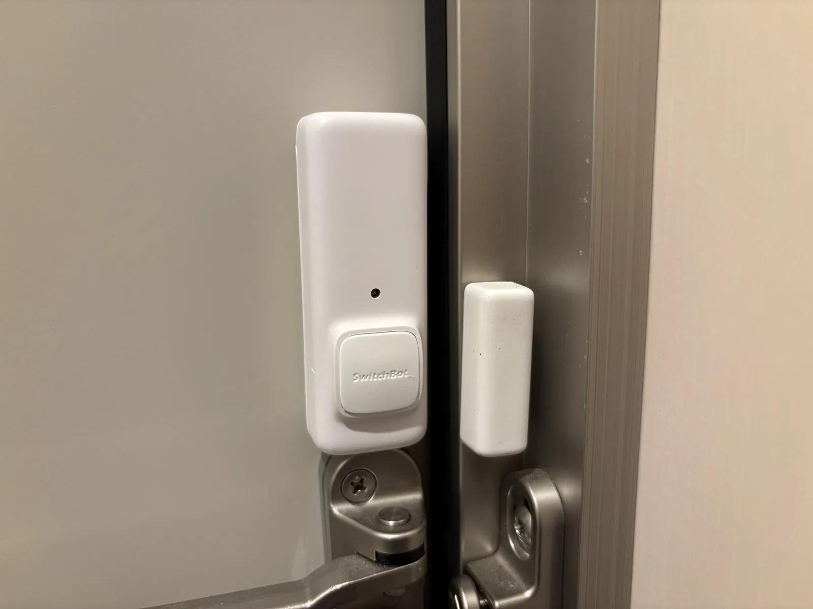 玄関ドアに設置したSwitchBot開閉センサー。左が本体（アクションボタン付き）、右がマグネット