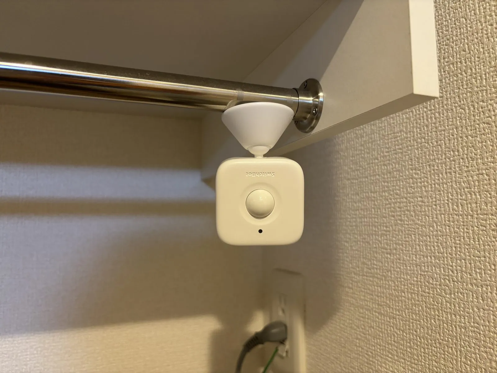 洗面所に設置したSwitchBot人感センサー。棚の下に付属の台座で吊り下げて、ドアの方向に向けている